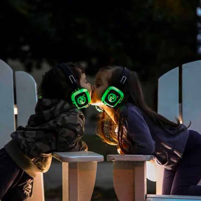 kids-silentexperience Twee meisjes met groene led-koptelefoons omhelzen elkaar 's avonds