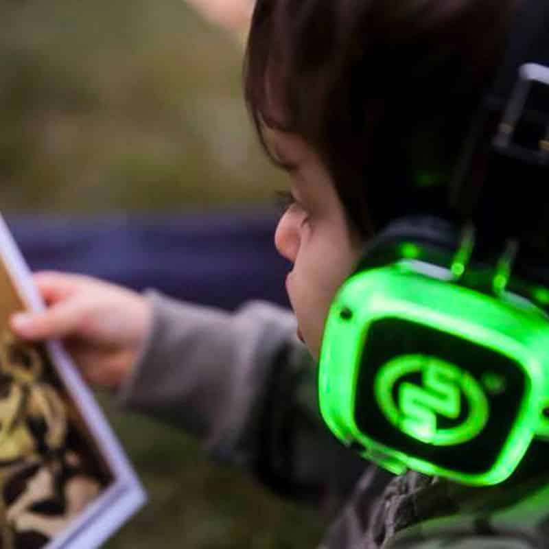 silentparty-bambini Jongen met groene silent disco koptelefoon bekijkt een ansichtkaart