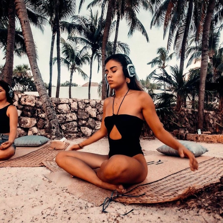 yoga-meditation Yogameditatie op een strand tussen palmbomen met draadloze koptelefoons